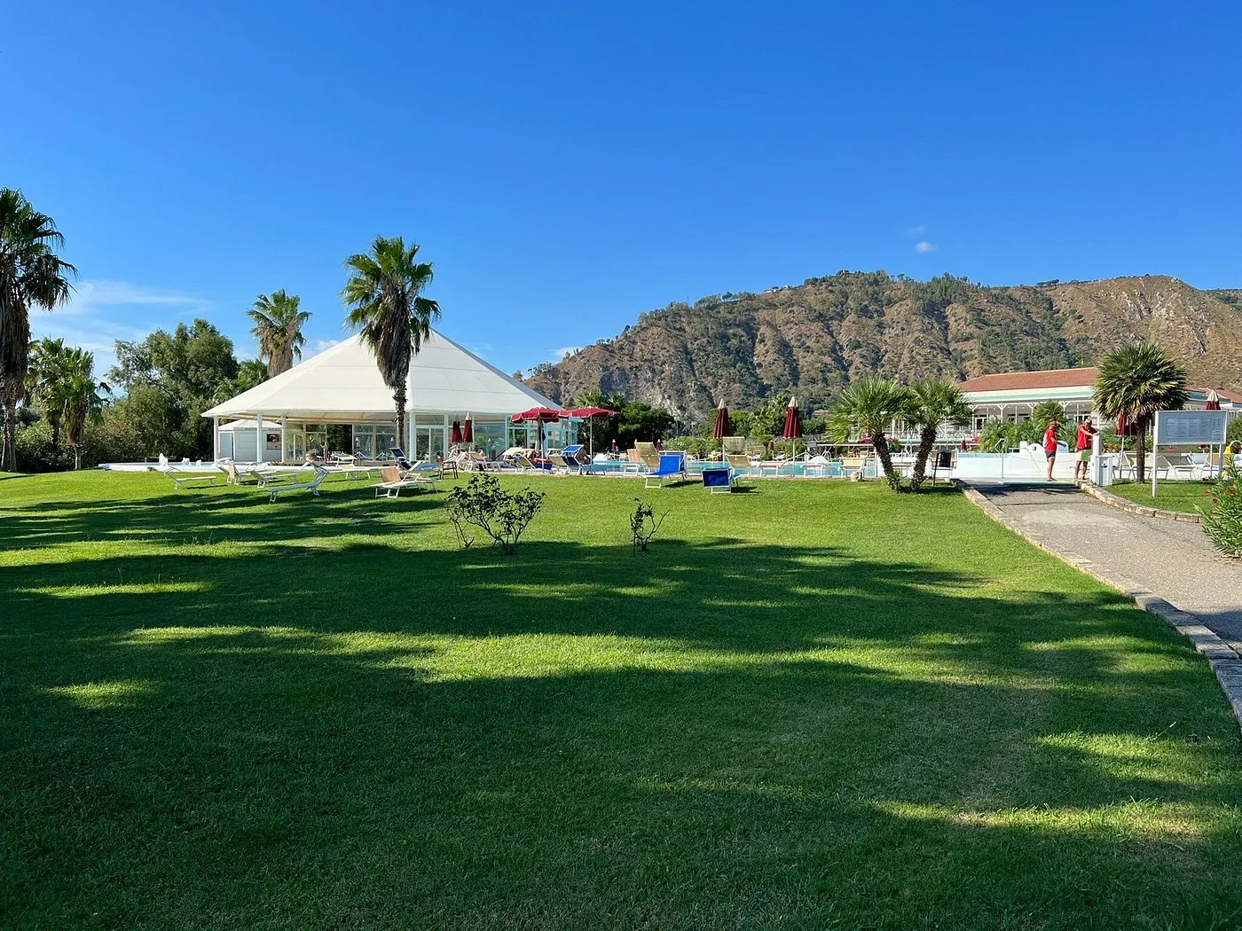 Prato verde del resort con gazebo bianco, lettini e montagne sullo sfondo
