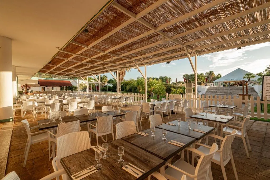 Ristorante all'aperto con tavoli in legno, sedie bianche e copertura in canniccio