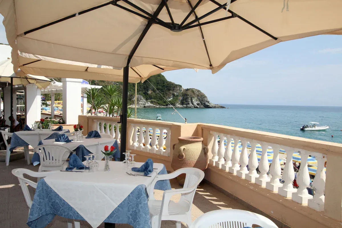 Terrazza ristorante con tavoli apparecchiati e ombrellone affacciata sul mare