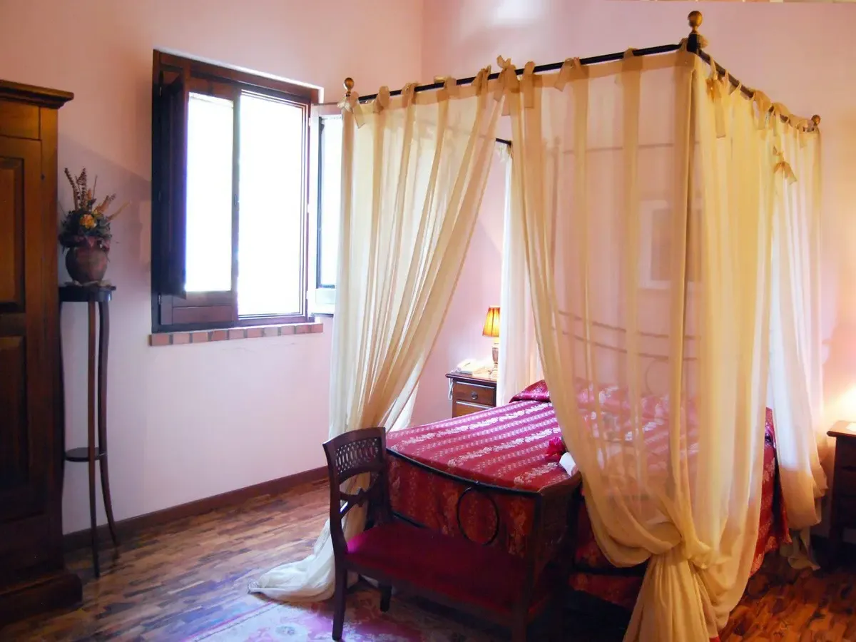 Camera con letto a baldacchino e tende beige, copriletto rosso e pavimento in legno