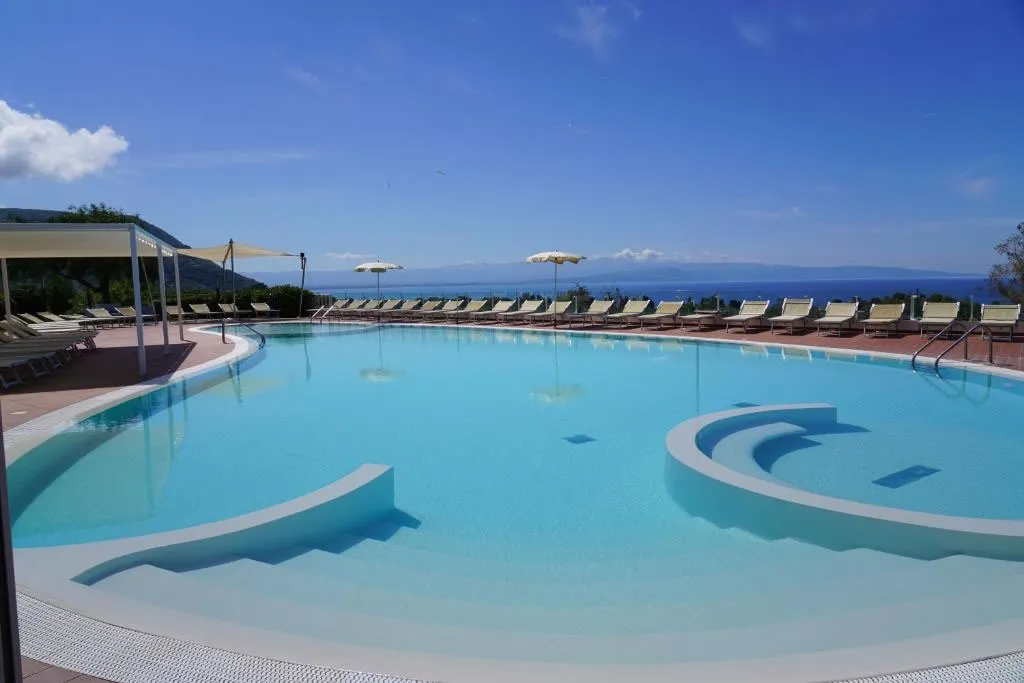Grande piscina azzurra con lettini, ombrelloni e vista mare all'orizzonte