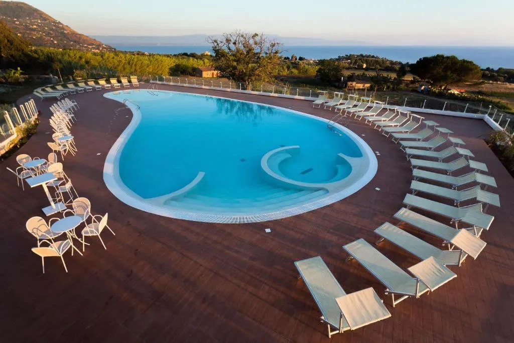 Piscina ovale con lettini e tavolini al tramonto con vista su mare e montagne