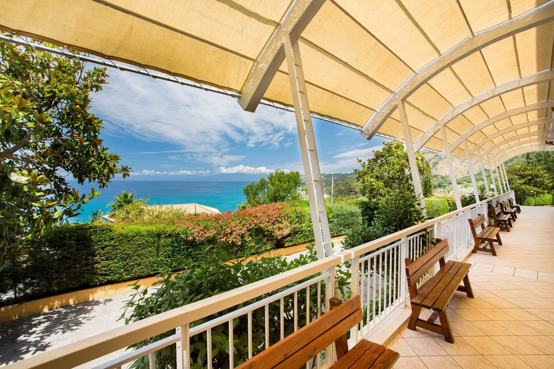 Veranda coperta con panche in legno e vista panoramica sul mare e giardino fiorito