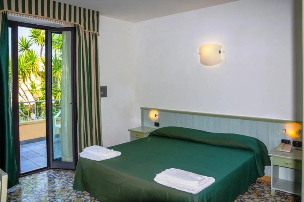 Camera con letto matrimoniale verde, tende a righe e balcone affacciato sul giardino