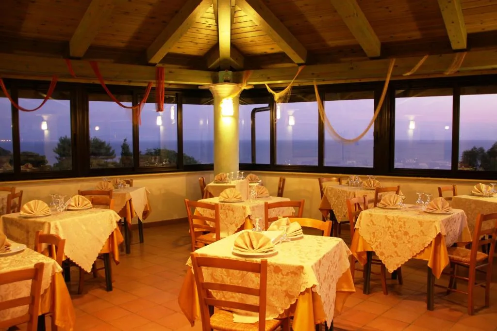 Sala ristorante panoramica al tramonto con tavoli apparecchiati e vetrate sul mare