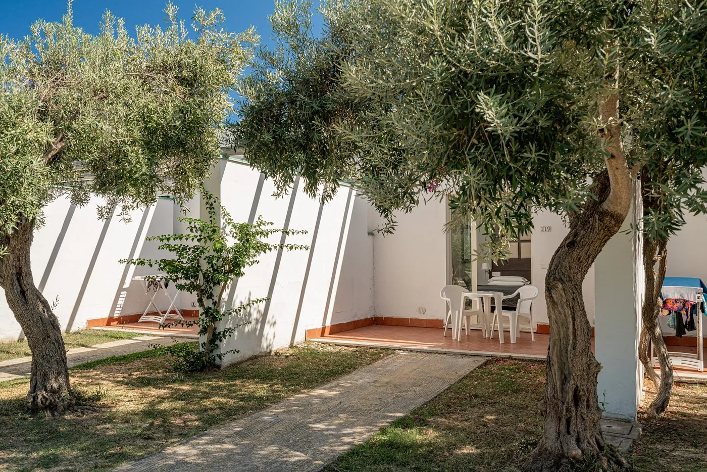 Patio esterno di un bungalow con tavolo e ulivi nel giardino