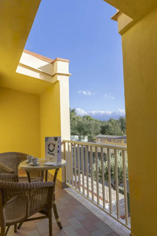 Balcone giallo con tavolino, sedie in vimini e vista su colline e vegetazione