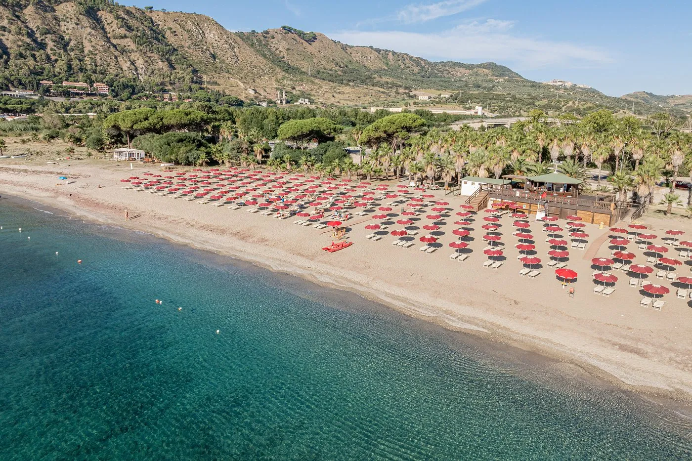 Spiaggia con ombrelloni rossi e neri, chiosco in legno e mare cristallino