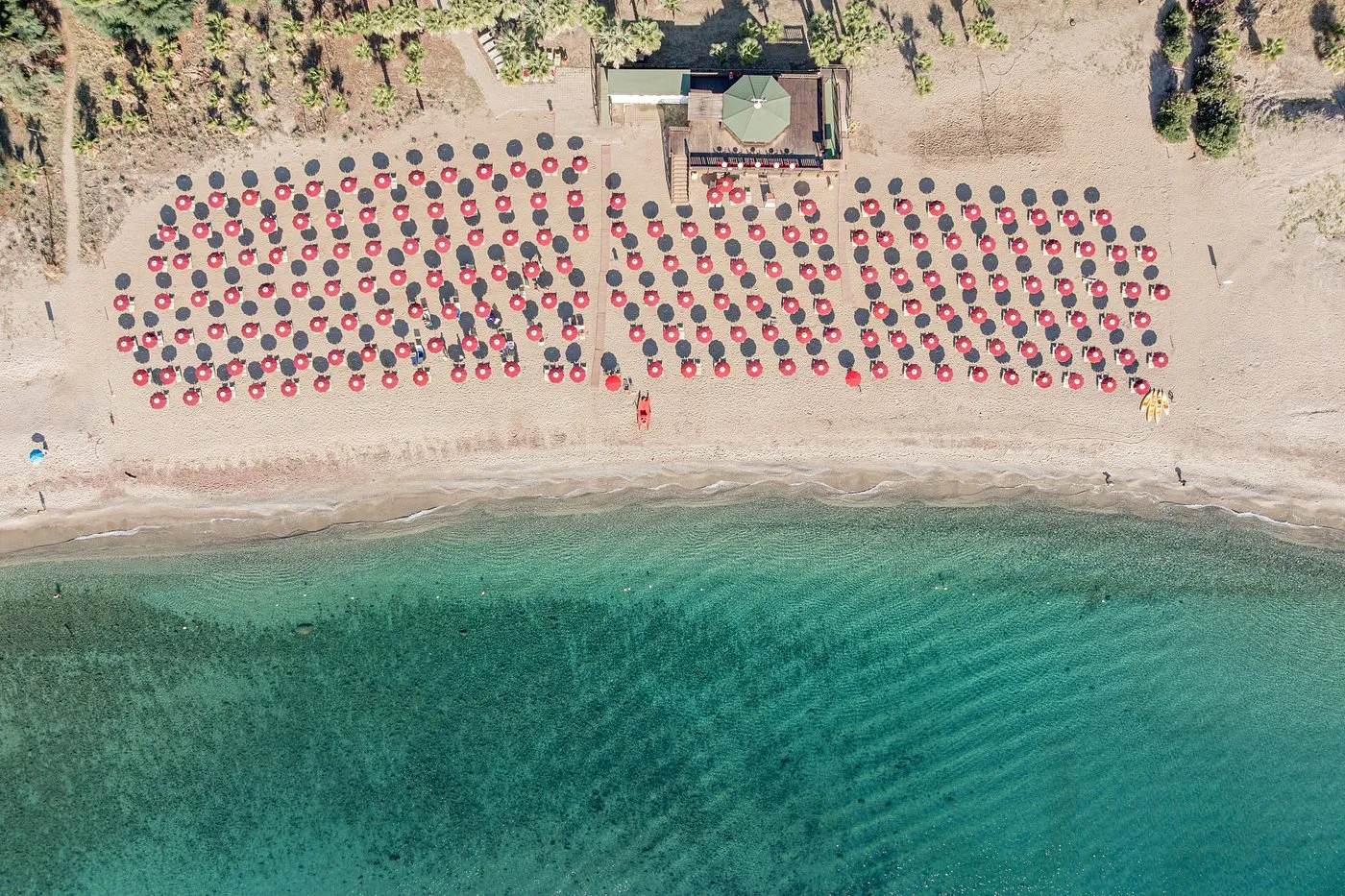 Vista aerea dall'alto della spiaggia con file di ombrelloni rossi e mare turchese