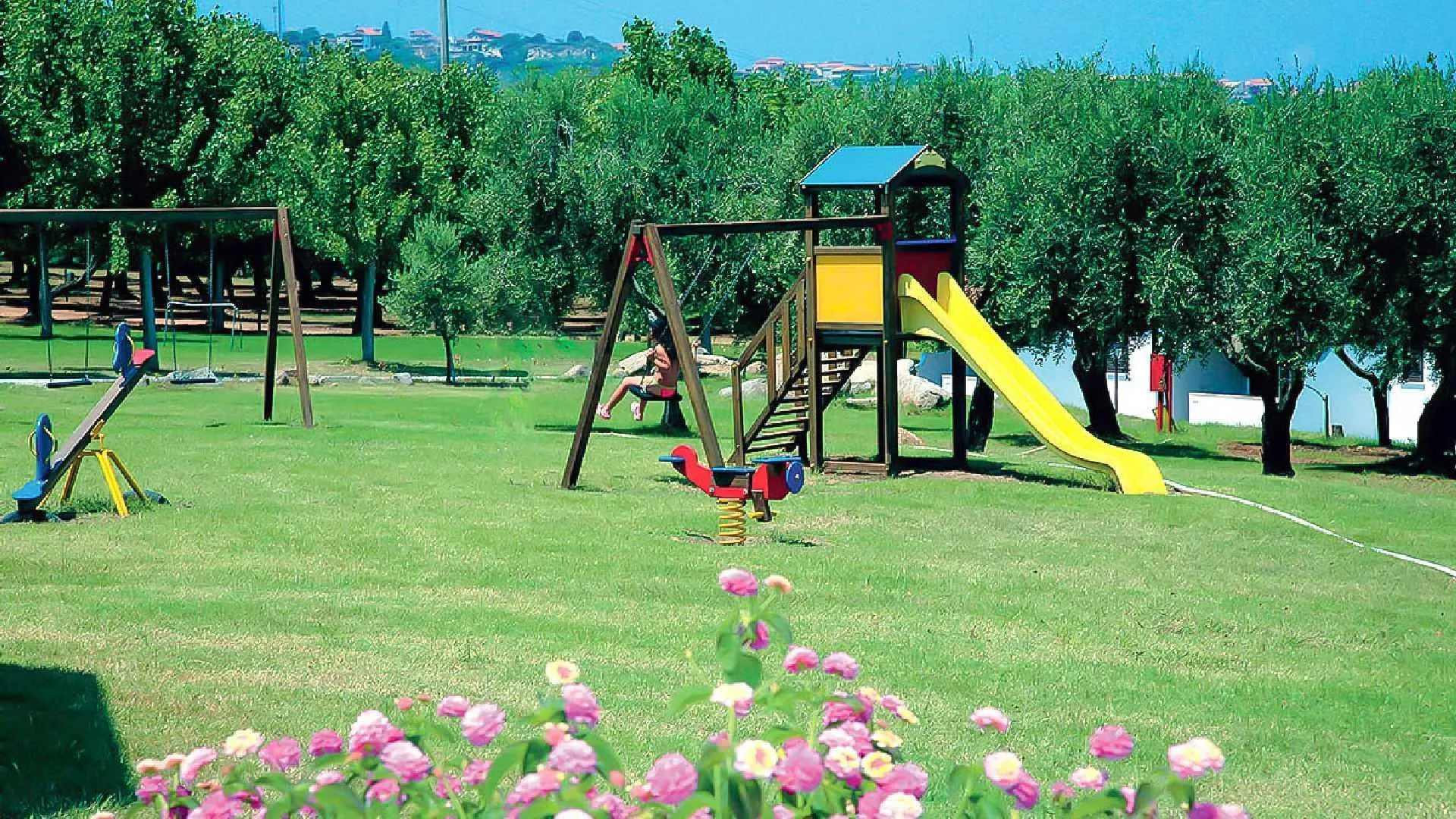 Parco giochi per bambini con scivolo giallo e altalene tra gli ulivi