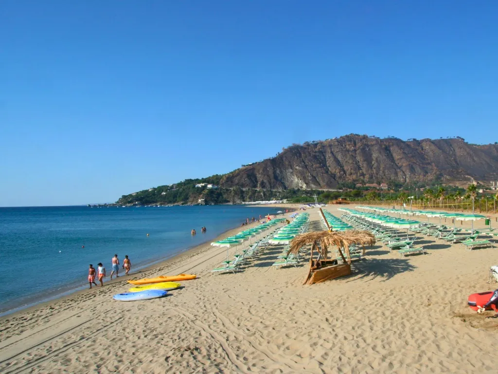 Spiaggia sabbiosa con lettini verdi, canoe colorate e promontorio sullo sfondo