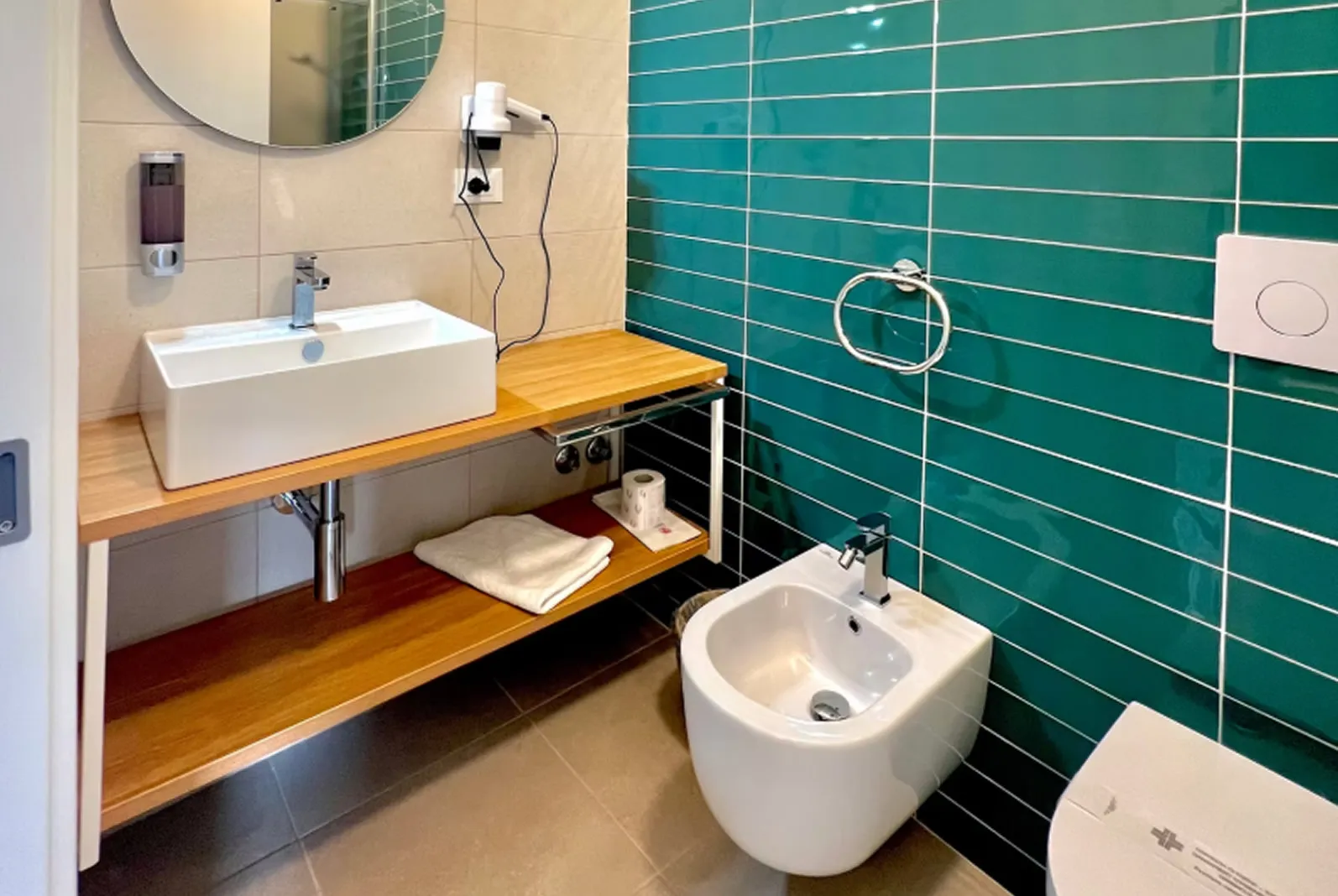 Bagno moderno con lavabo su mensola in legno, bidet e piastrelle verdi
