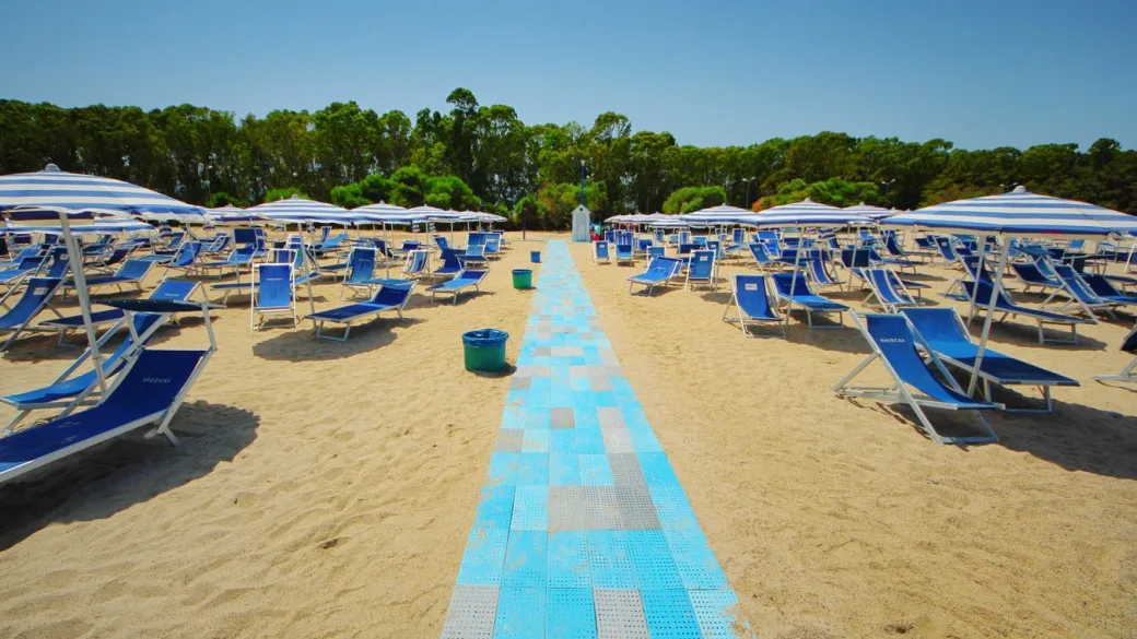 Spiaggia attrezzata con ombrelloni a righe e passerella azzurra sulla sabbia