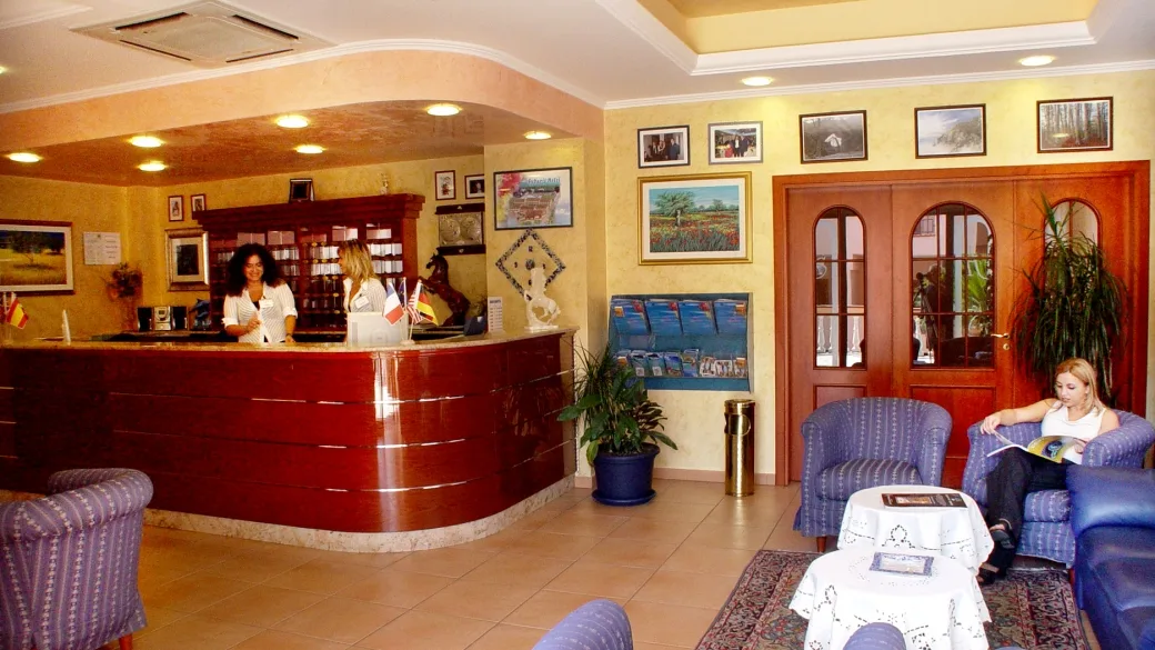 Reception dell'hotel con bancone in legno, personale di accoglienza, poltrone e zona lounge