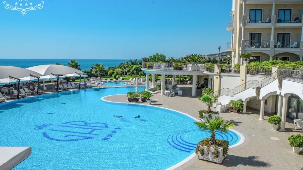 Piscina a forma curva con palme e terrazza vista mare