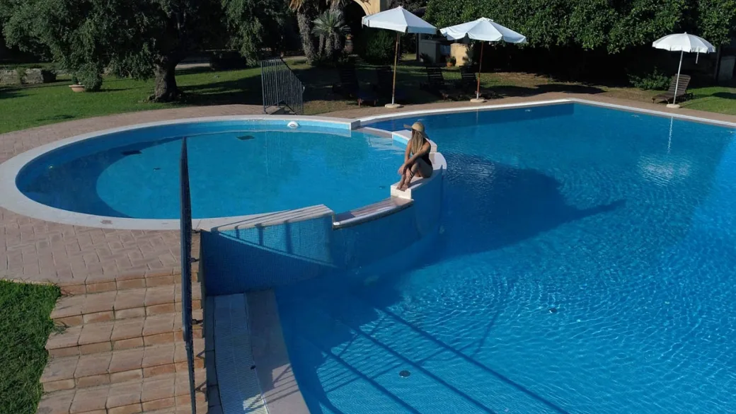 Dettaglio della piscina con scalinata, ombrelloni e persona seduta sul bordo