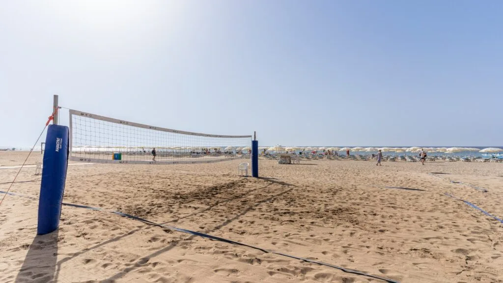 Campo di beach volley vuoto sulla spiaggia sabbiosa con ombrelloni bianchi e cielo sereno.