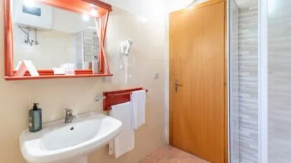 Bagno con lavabo bianco, specchio con cornice arancione, asciugacapelli a muro e porta in legno chiaro.