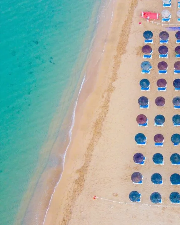 Spiaggia con ombrelloni disposti in file ordinate e salsa azzurra calma vista dall'alto.