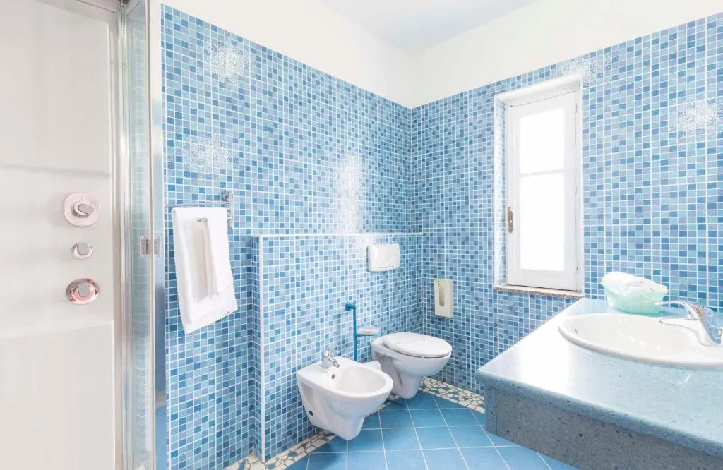 Bagno con rivestimento a mosaico azzurro, doccia, sanitari, bidet e lavabo